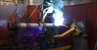 Robotic arm welding a large metal component on an automated manufacturing line in an industrial factory.