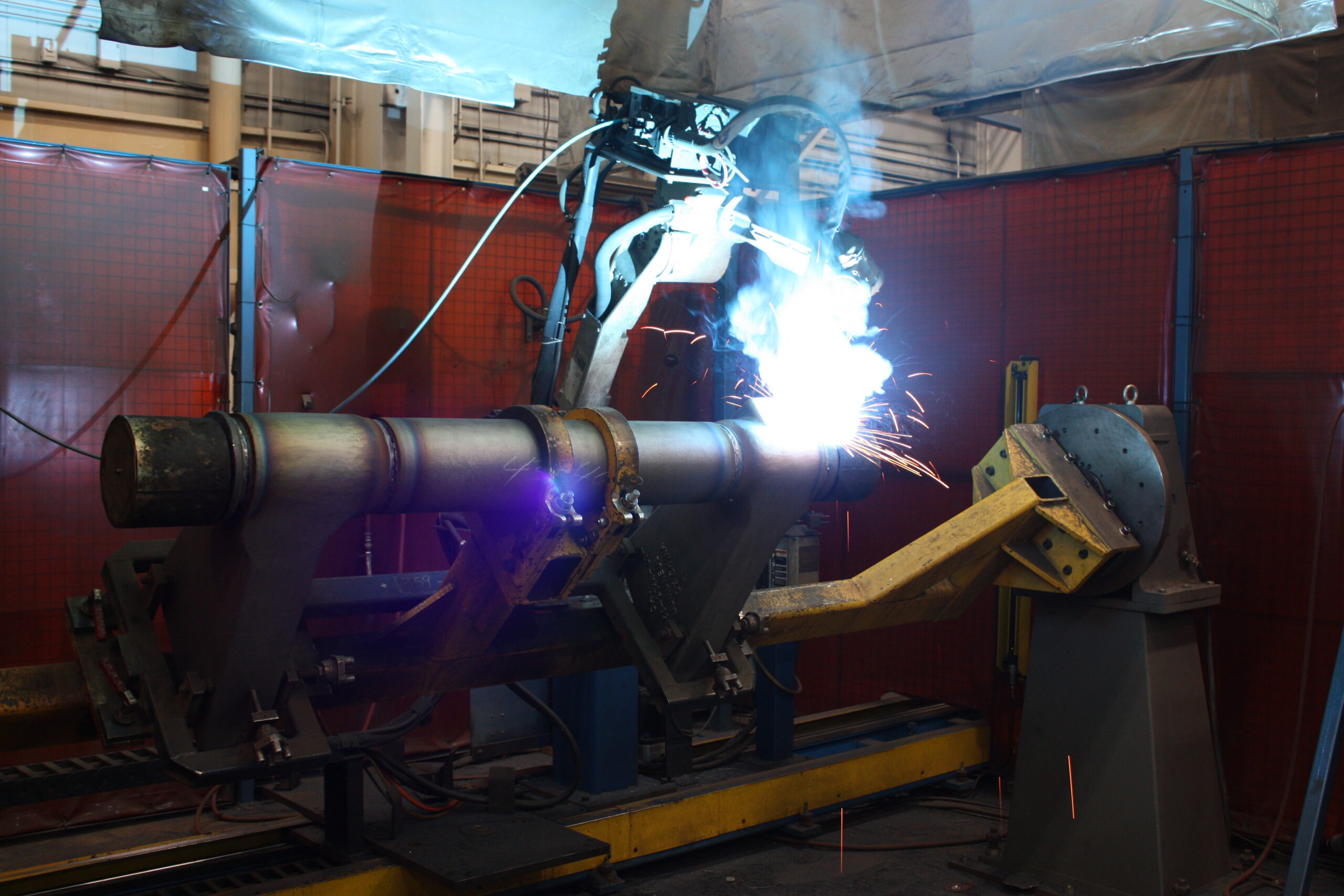 Robotic arm welding a large metal component on an automated manufacturing line in an industrial factory.