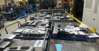 fabrication ERP features: cut sheet metal parts staged on work tables with paper job travelers in a fabrication shop