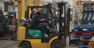 Forklift operator moving palletized parts in an automotive supplier manufacturing facility.