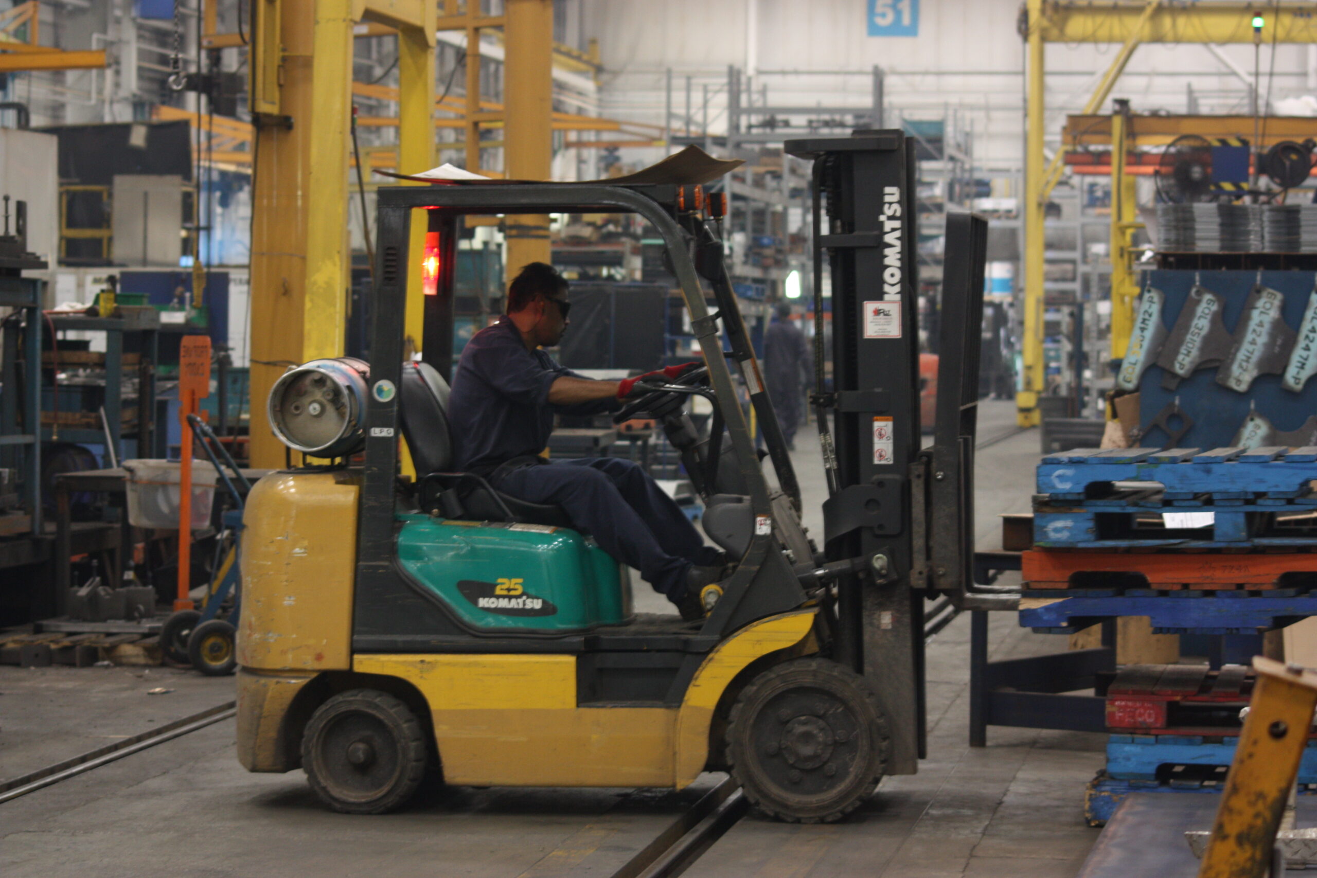 Forklift operator moving palletized parts in an automotive supplier manufacturing facility.