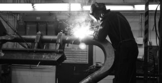 Black and white photo of a welder at work in a fabrication shop, illustrating AI for small manufacturers